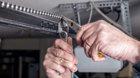 Man works with pliers to repair a garage door opener chain Tools are used to work on a garage door opener chain